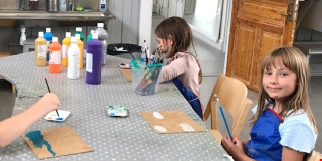 Tre barn sitter och målar med färg vid ett bord.