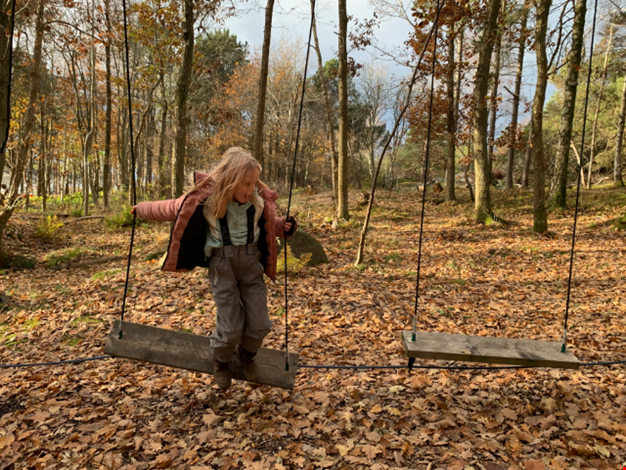 Flicka leker på låghöjdsbana i skogen.